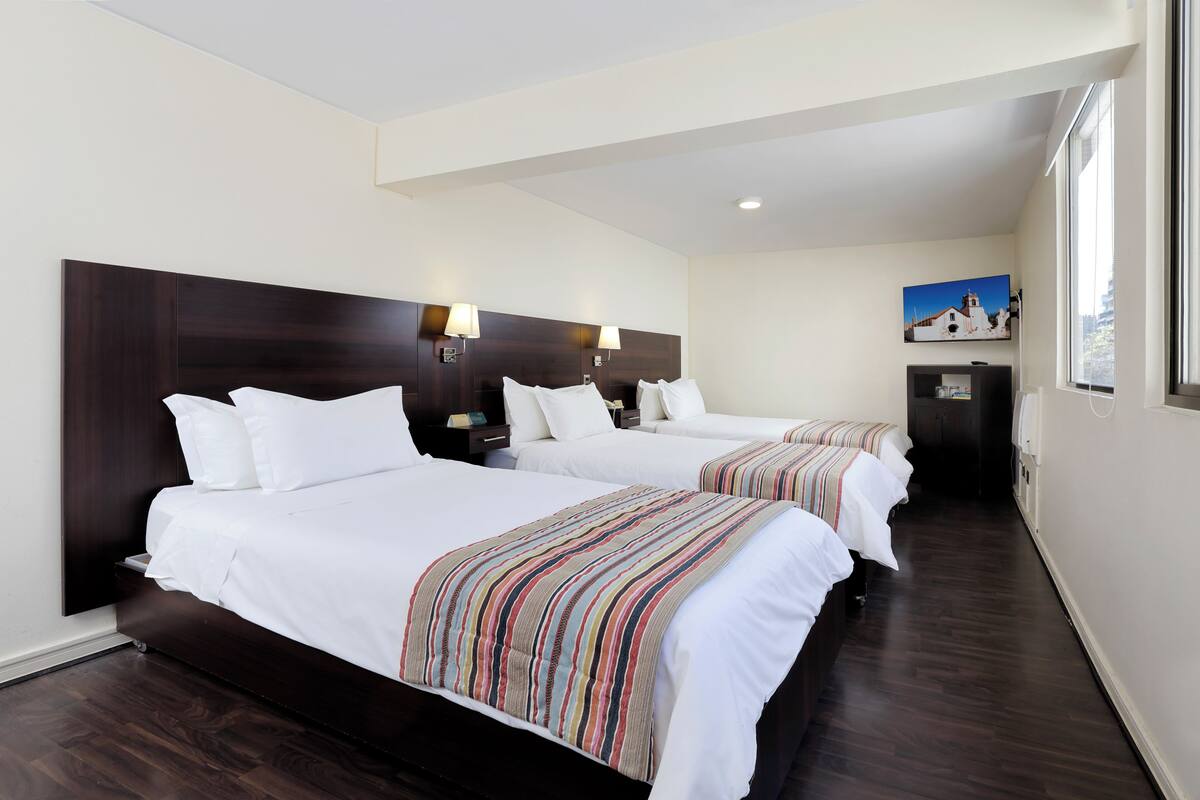 A hotel room with two beds, dark wood headboards, white bedding, and a painting on the wall.