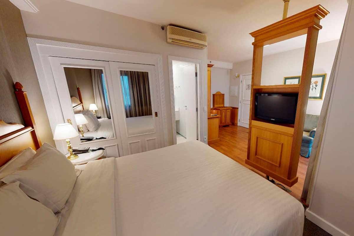 Une chambre d’hôtel avec un grand lit, une télévision, une armoire en bois et un miroir.