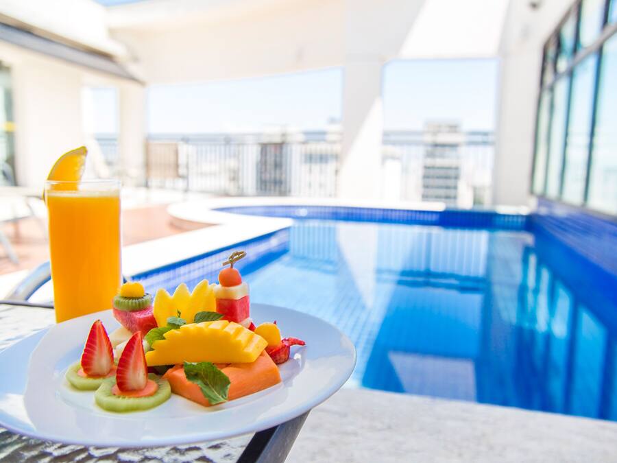 Una mesa de comedor con un plato de fruta y un vaso de jugo de naranja junto a una piscina.