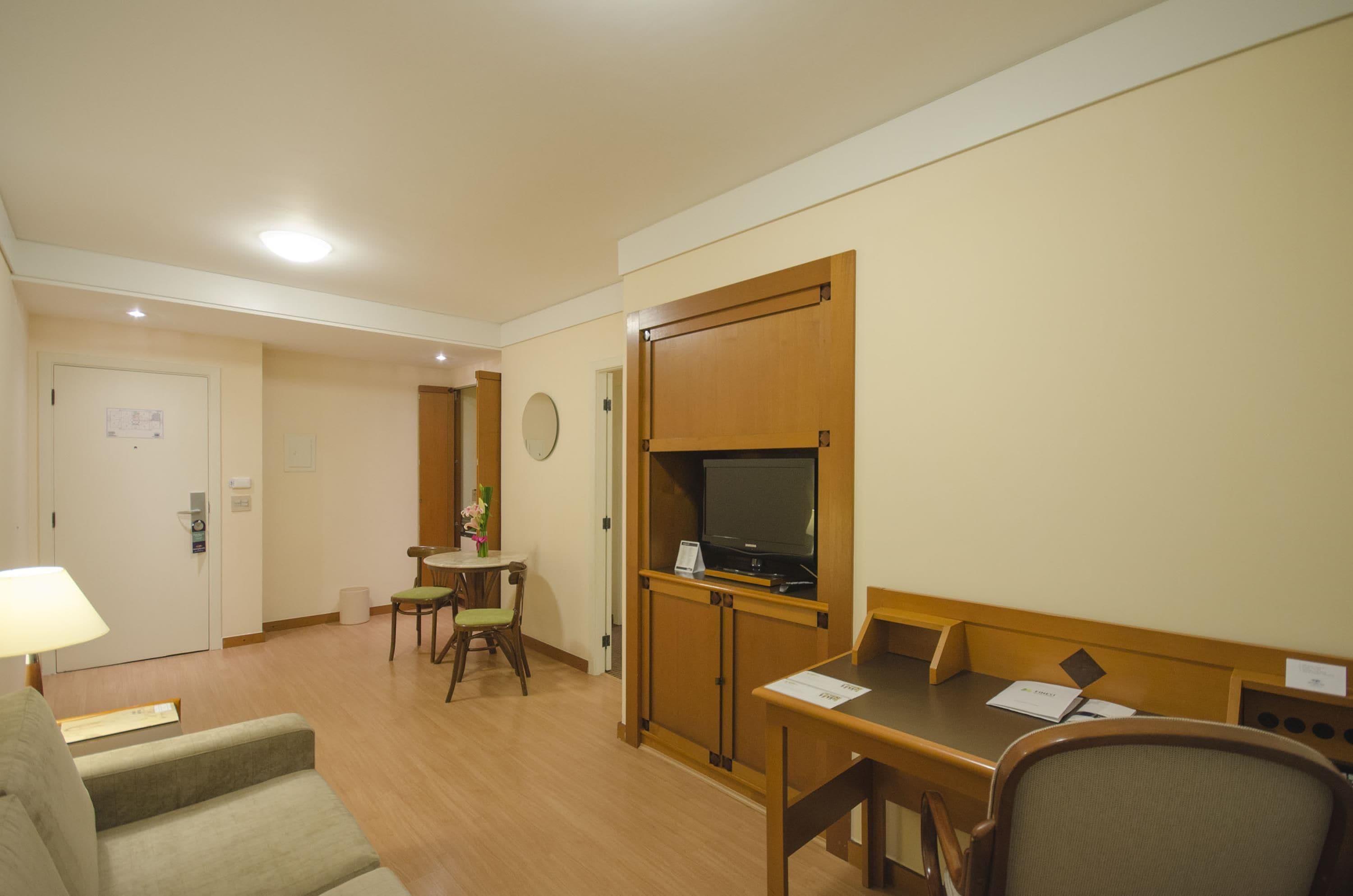A hotel room with a wooden desk, a television, a small table with a chair, and a sofa.