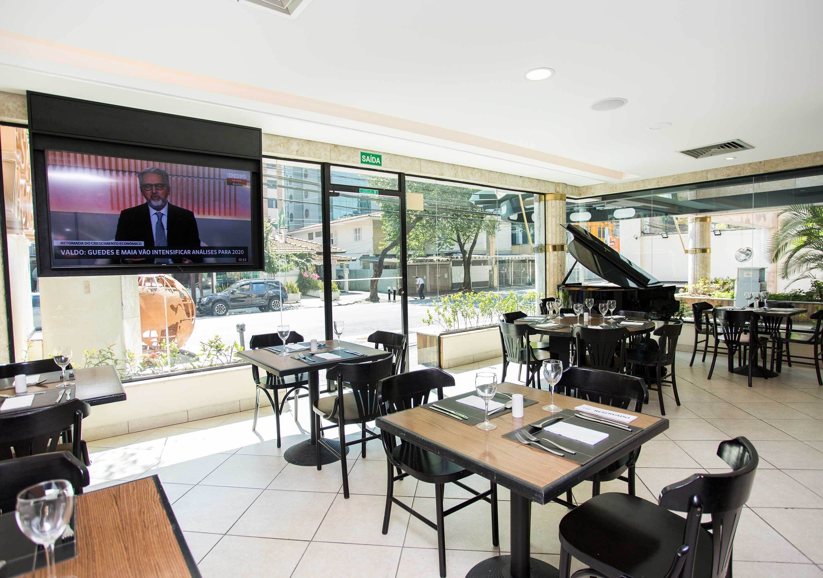 Un restaurante con mesas, sillas, una pantalla de televisión y vistas al exterior.
