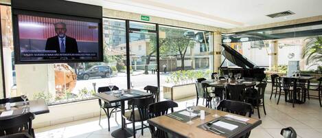 Un restaurante con mesas, sillas, una pantalla de televisión y vistas al exterior.