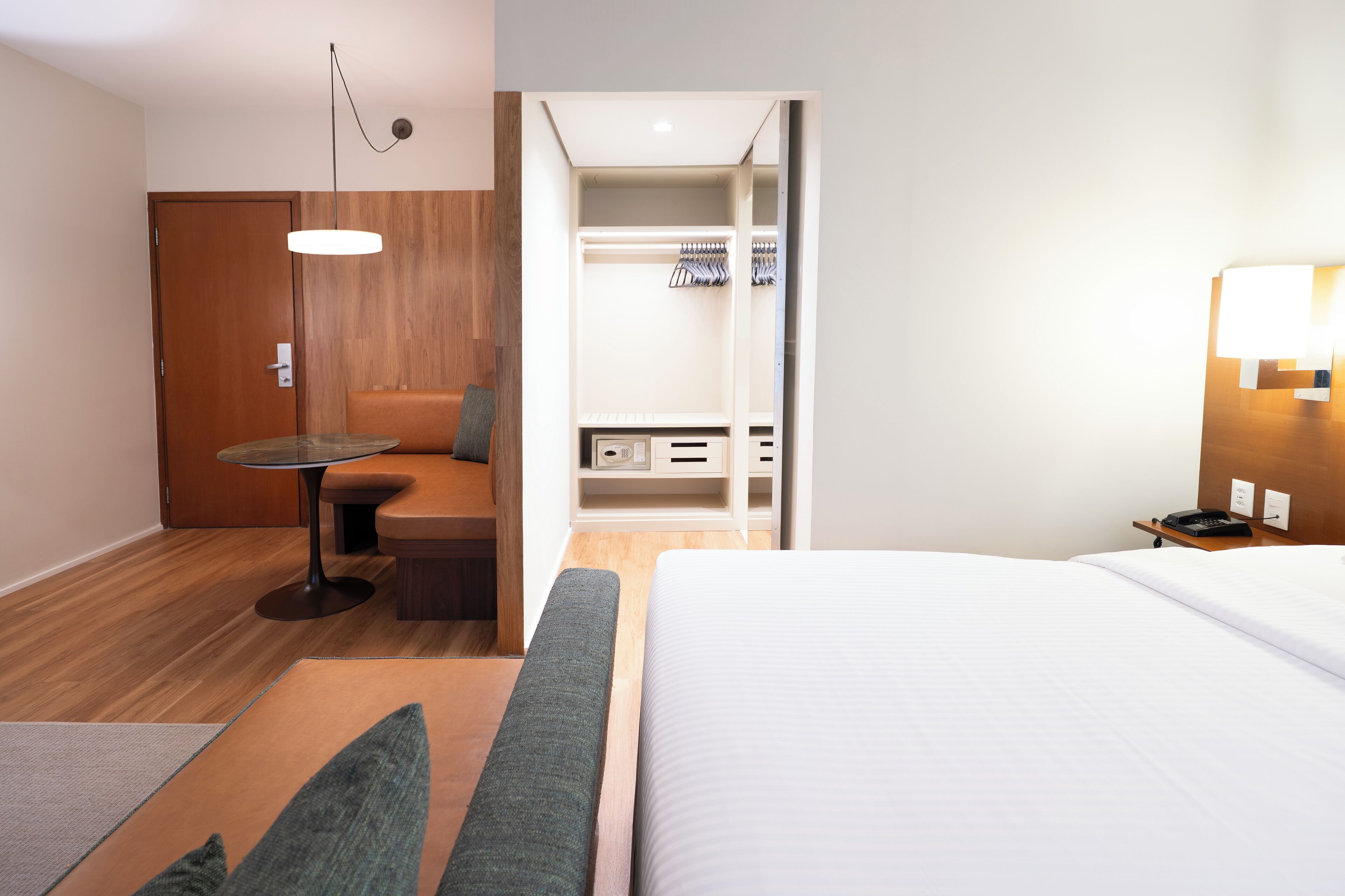 Una camera d'albergo con un letto, un'area salotto con tavolo e sedie, un armadio e un comodino con una lampada.