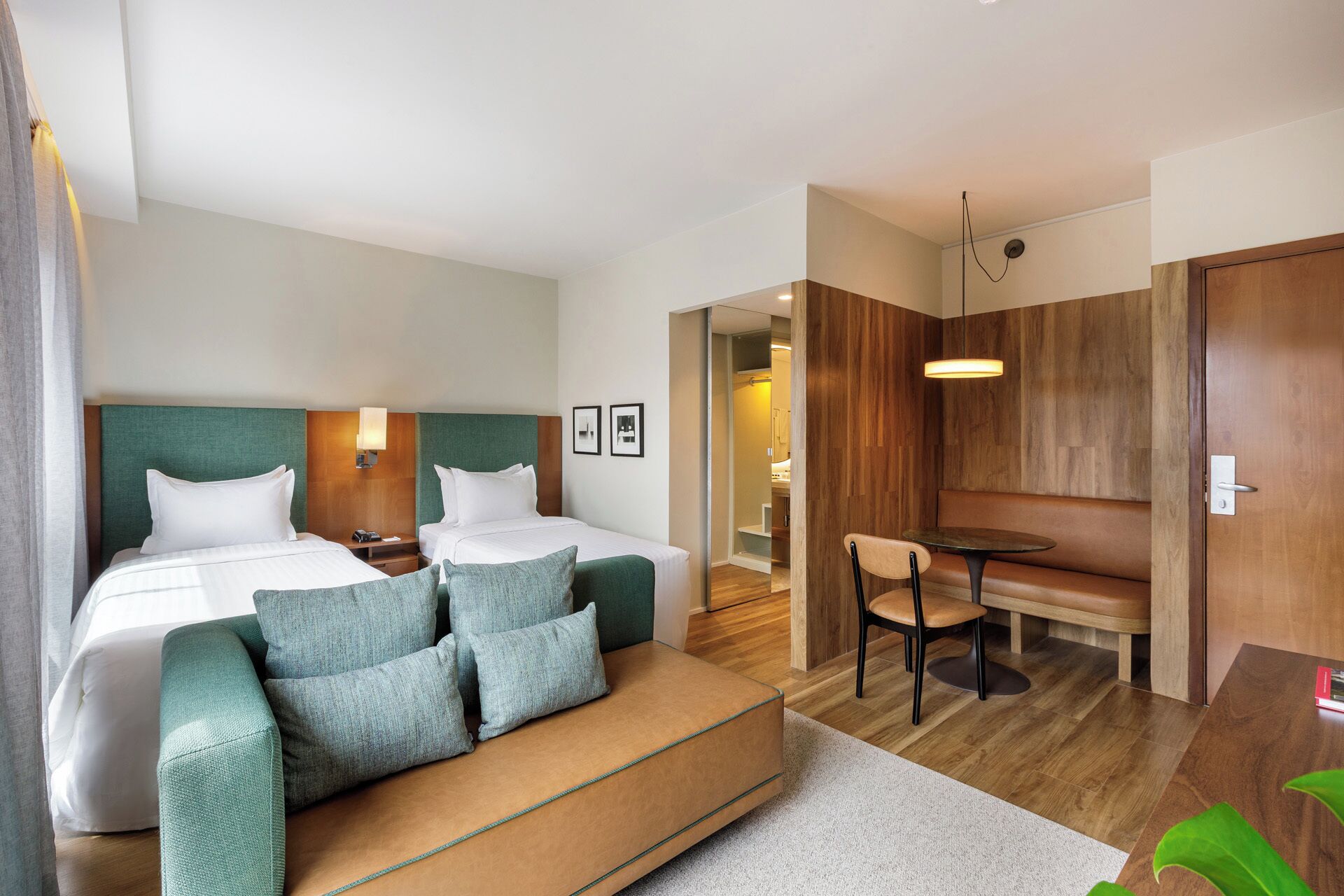 A hotel room with a bed, two bedside tables, a sofa, a dining table, and a small kitchen area.