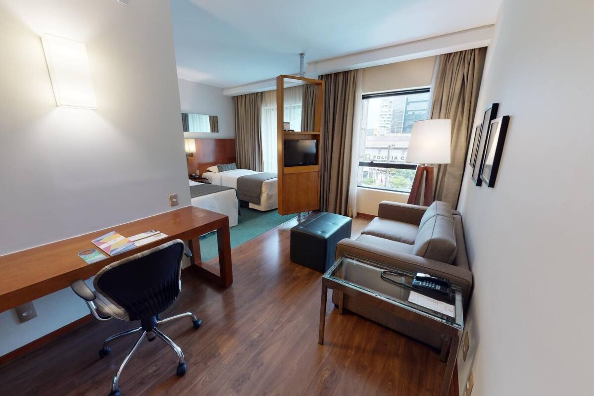 A hotel room with a wooden desk, a sofa, a TV, and a bed.