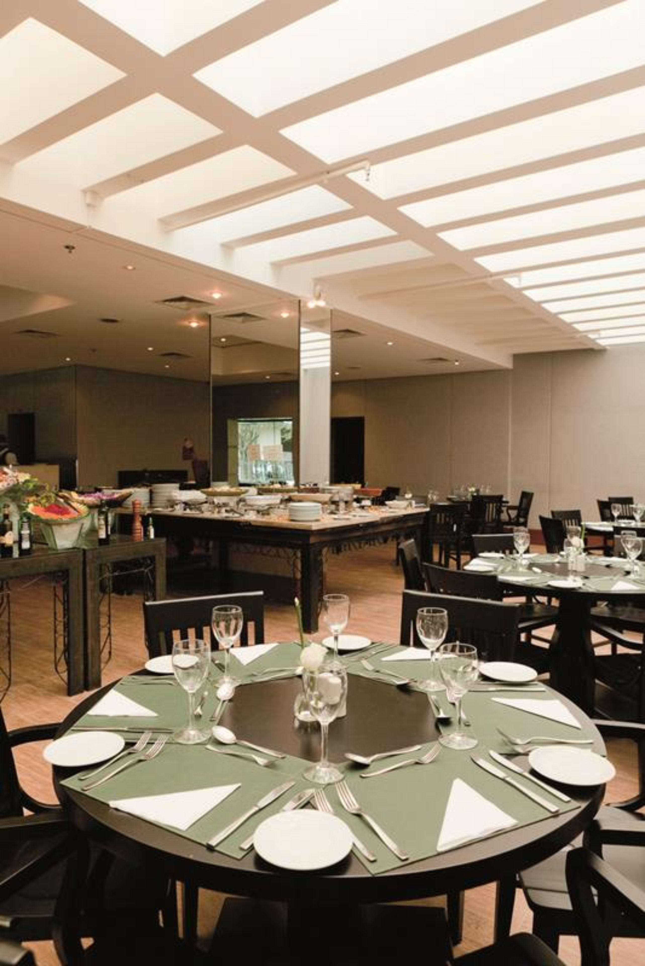 A dining area with round tables set for service, a buffet line, and a high ceiling with skylights.