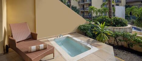 Eine Lounge-Ecke mit Korbstuhl, kleinem Pool und Blick auf ein Resortgebäude mit Balkonen und Palmen.