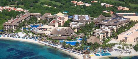 Vista aérea de un resort con varias edificaciones, una playa y un área de piscina.