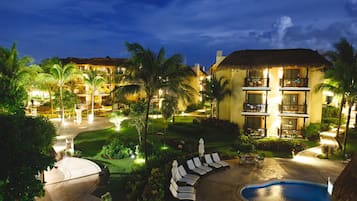 Um resort com piscina, espreguiçadeiras e um jardim bem iluminado à noite.