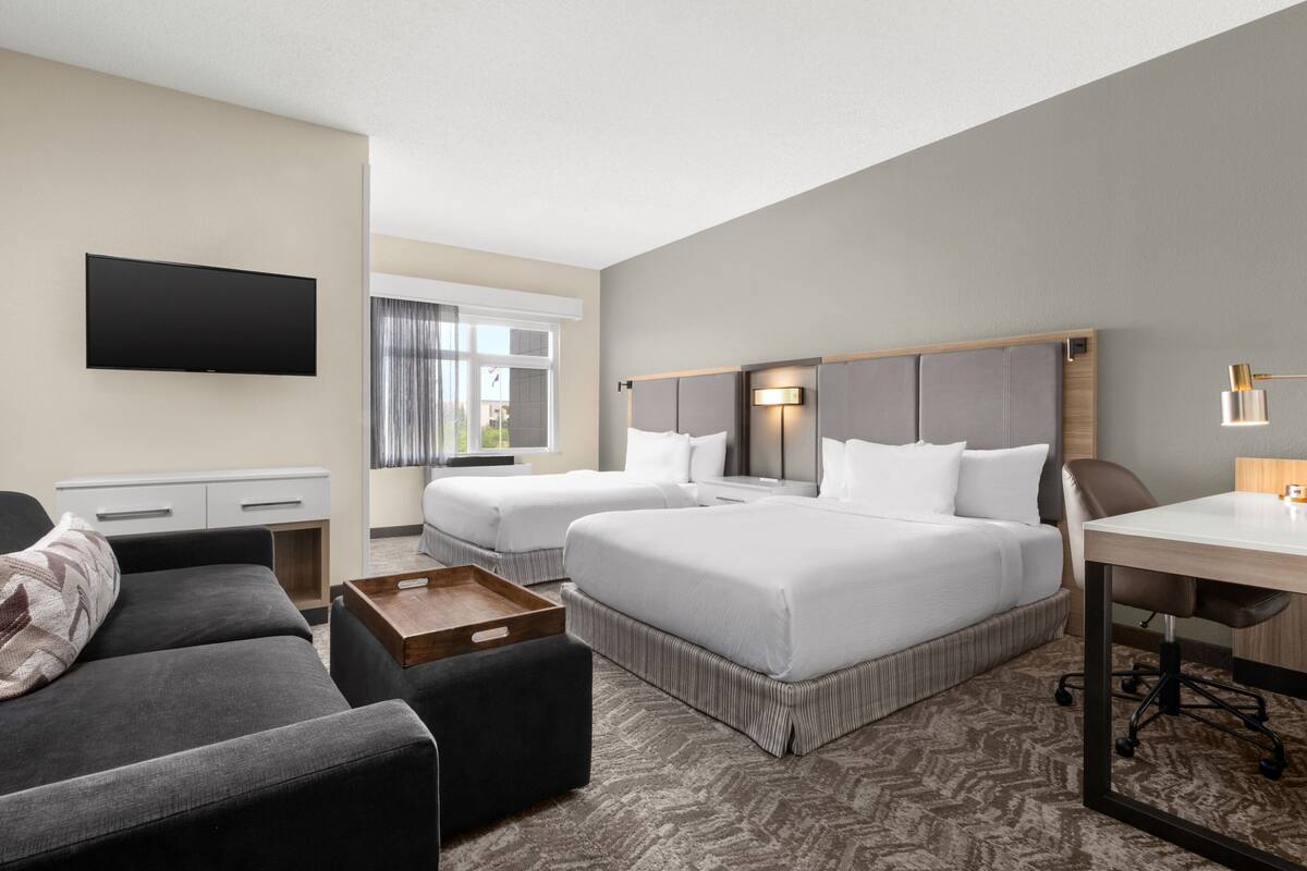 A hotel room with two beds, a desk, a TV, and a sofa.