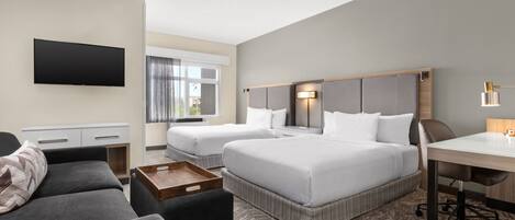 A hotel room with two beds, a desk, a TV, and a sofa.