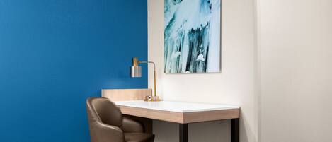 A corner office with a desk, chair, and a wall-mounted lamp.