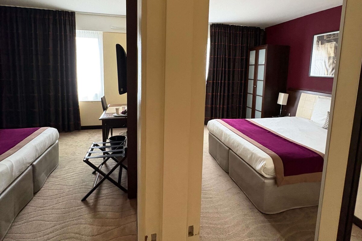 Una camera d'albergo con due letti, una scrivania e una sedia.
