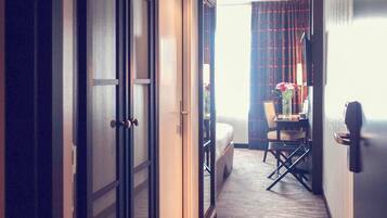 Un couloir d’hôtel avec un lit, une table ornée de fleurs et une chaise.