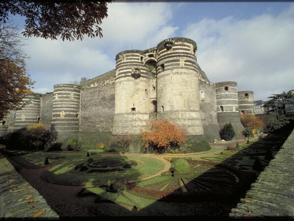 Un castillo histórico con varias torres redondas y un jardín bien cuidado con diseños geométricos.