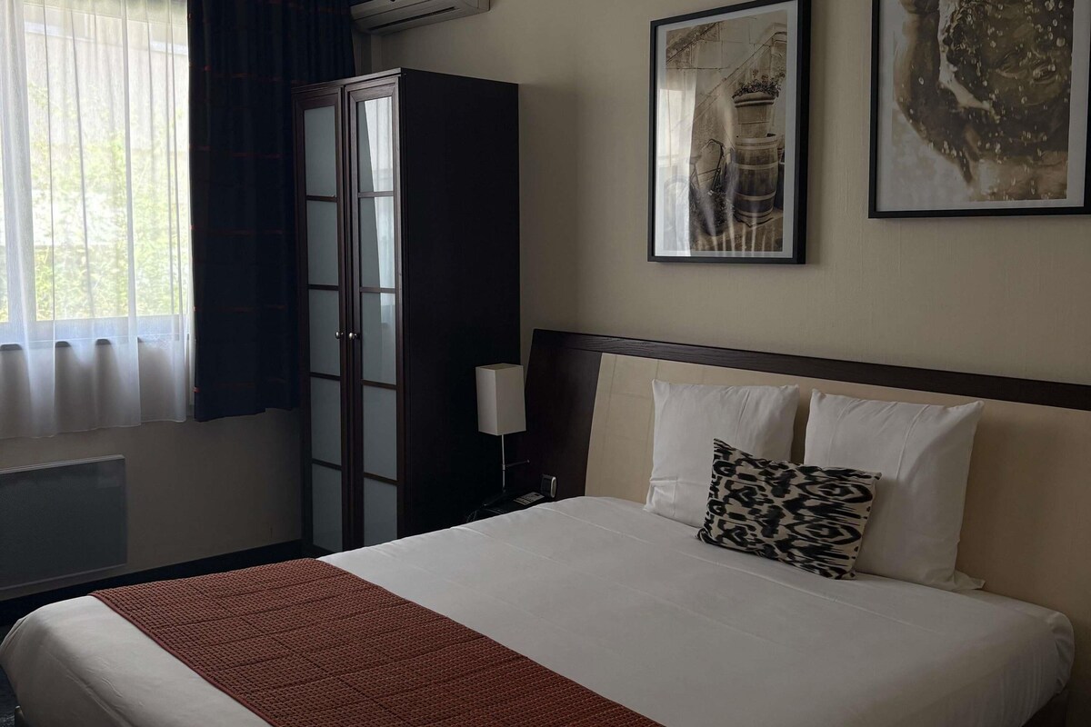 Una camera d'albergo con un letto, un armadio, un termosifone e una finestra con tende.