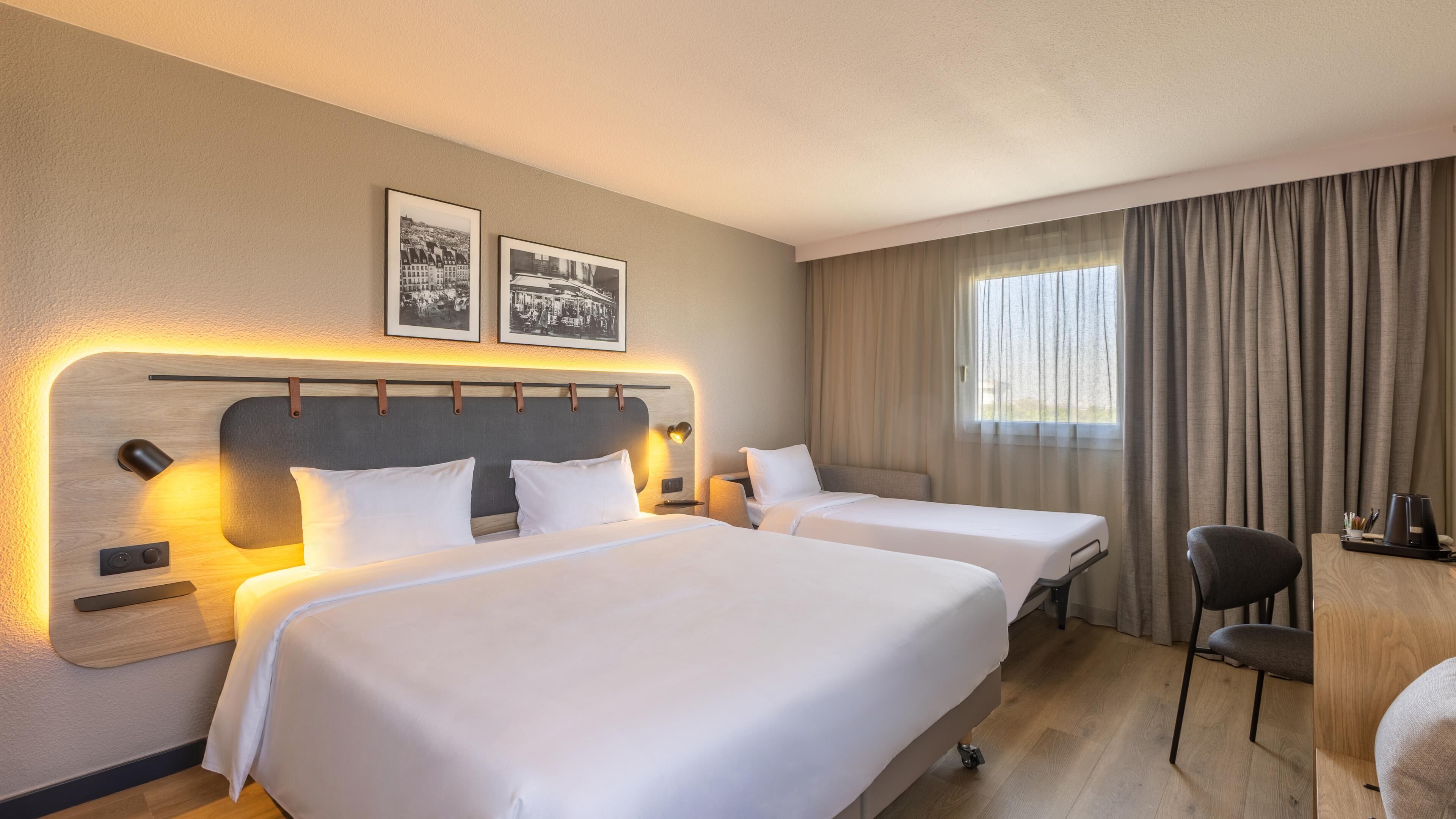 A hotel room with two beds, a desk, a chair, and a window with curtains.