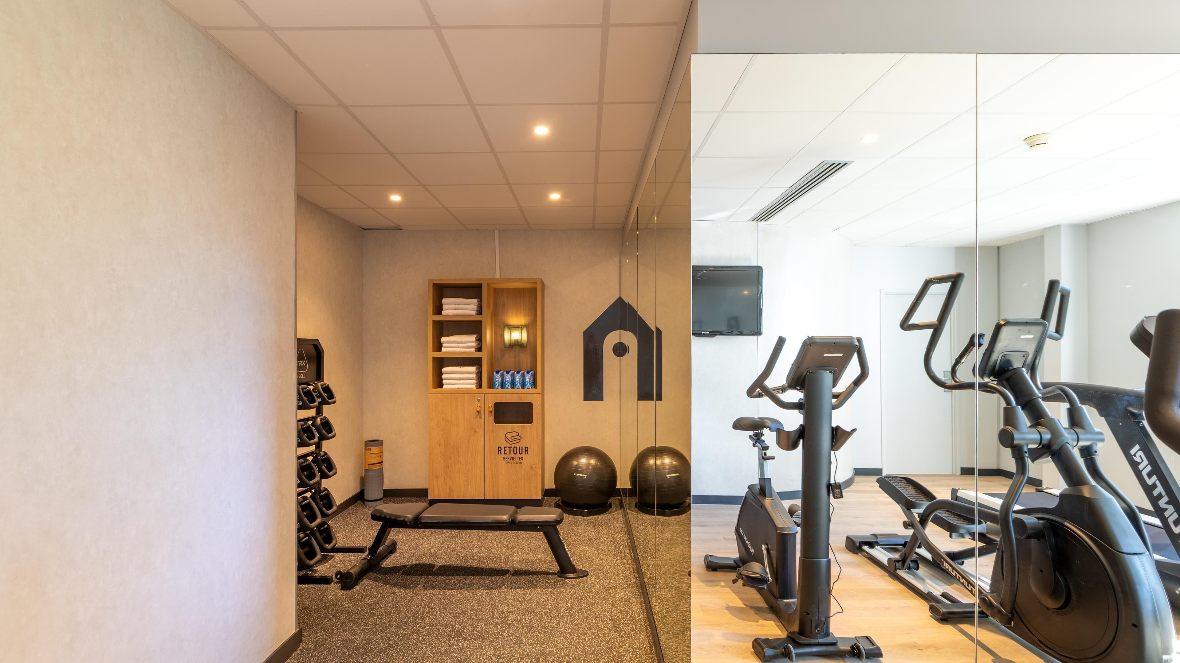 A gym with exercise equipment, a reception desk, and a wall-mounted TV.