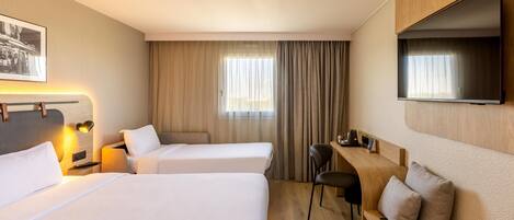 A hotel room with two beds, a desk, a chair, a TV, and a window with curtains.
