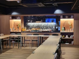 A modern dining area with a long wooden table, chairs, and a kitchen counter with a marble backsplash.