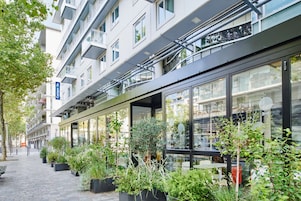 A modern building with large windows, outdoor seating, and potted plants.