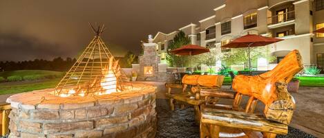 A stone fire pit with a teepee structure, wooden benches, and a stone fireplace.