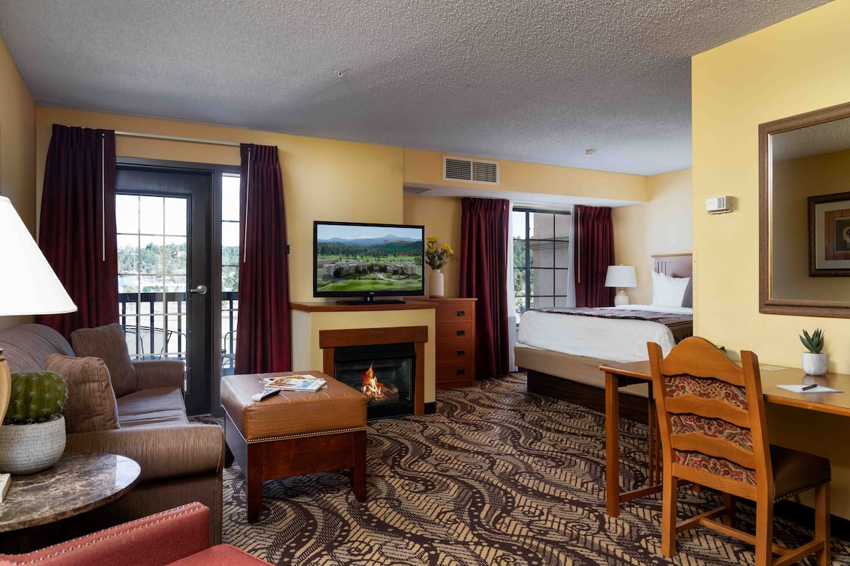 A hotel room with a sofa, a small table with a cactus, a television, a fireplace, a bed, a desk, and a chair.