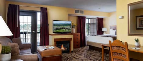 A hotel room with a sofa, a small table with a cactus, a television, a fireplace, a bed, a desk, and a chair.