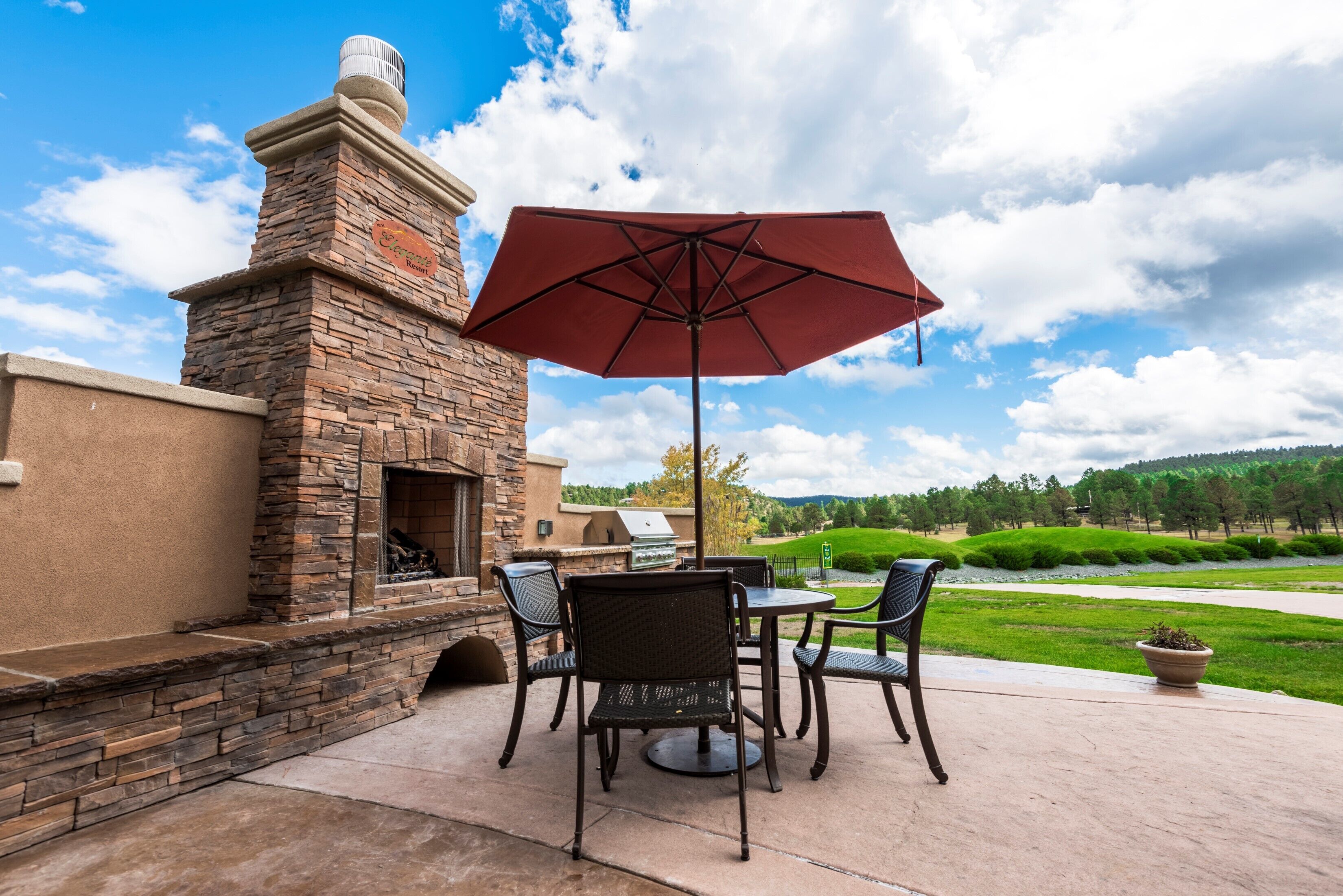 An outdoor patio with a stone fireplace, a grill, and a table with chairs.