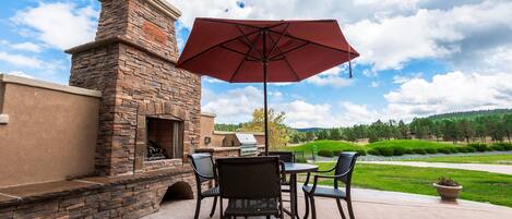 An outdoor patio with a stone fireplace, a grill, and a table with chairs.