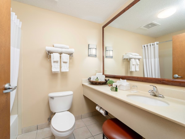 A bathroom with a toilet, sink, and mirror. There are towels hanging on a rack and a shower curtain.