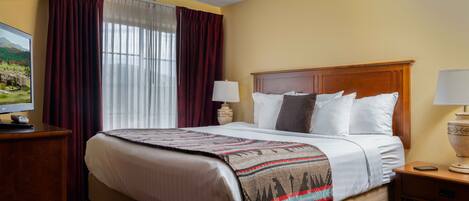 A hotel room with a large bed, two bedside tables, a television, and a window with curtains.