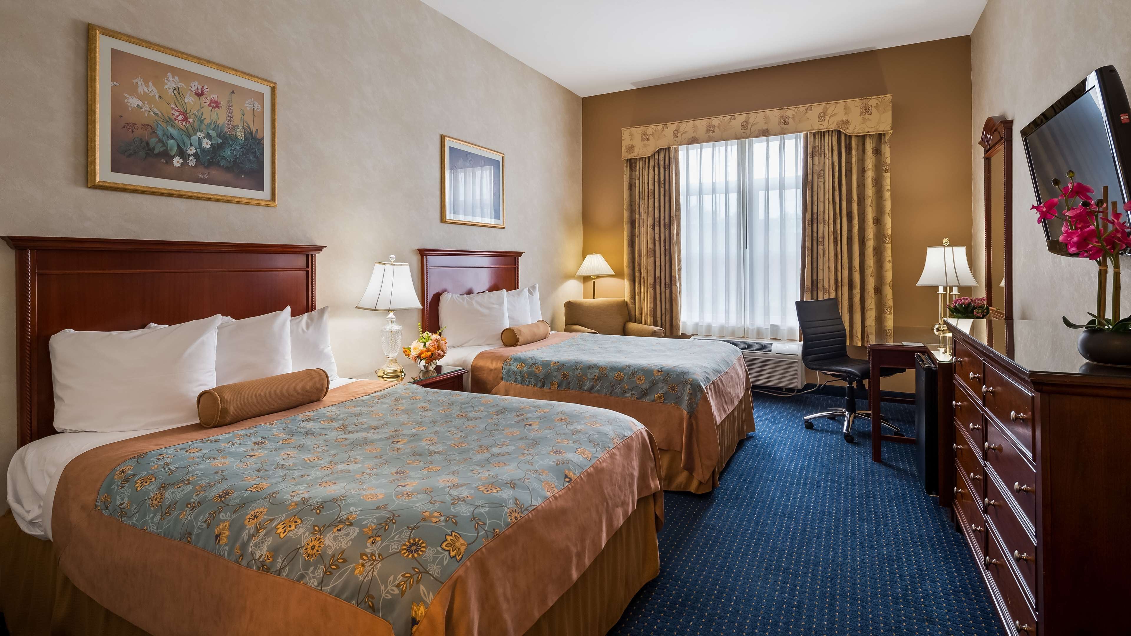 A hotel room with two beds, a desk, a chair, a dresser, and a large mirror.
