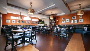 A restaurant interior with wooden tables, black chairs, and orange walls. - Best Western Plus Mentor-Cleveland Northeast (Mentor)