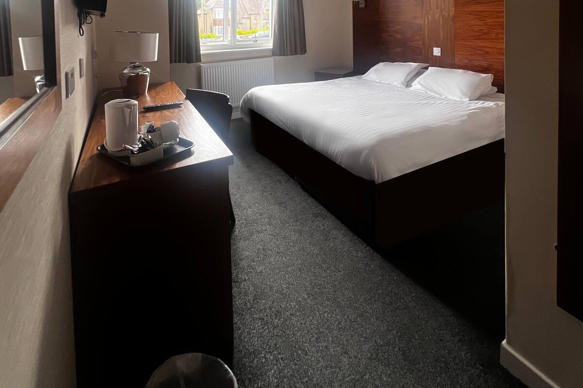 Ein Hotelzimmer mit Bett, Schreibtisch, Stuhl, Lampe und einem Fenster mit Vorhängen.