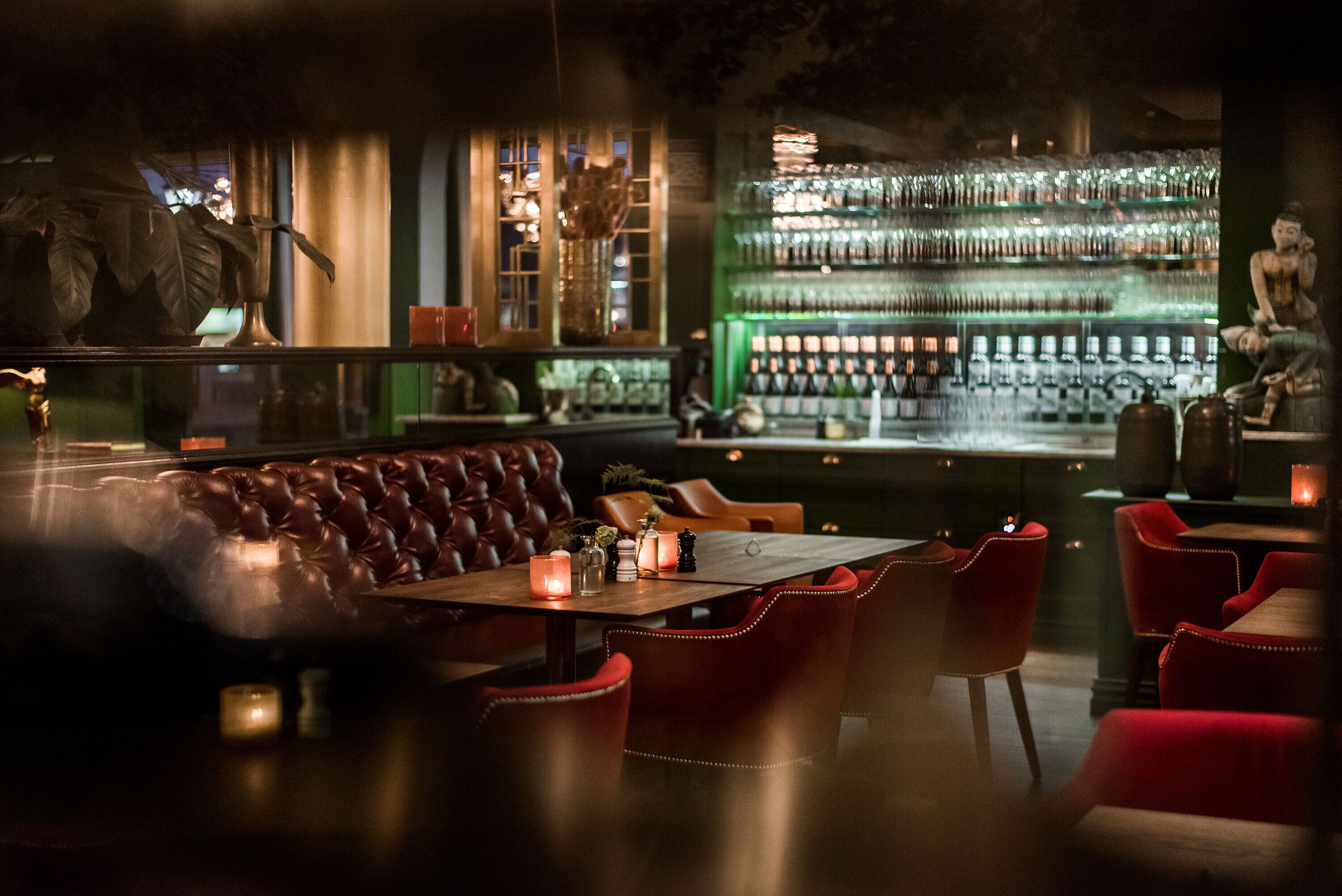 A dimly lit bar with a leather booth, red chairs, and a well-stocked bar counter.