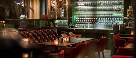 A dimly lit bar with a leather booth, red chairs, and a well-stocked bar counter.