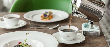 Una mesa con dos platos de comida y dos tazas de café, una de ellas siendo servida.