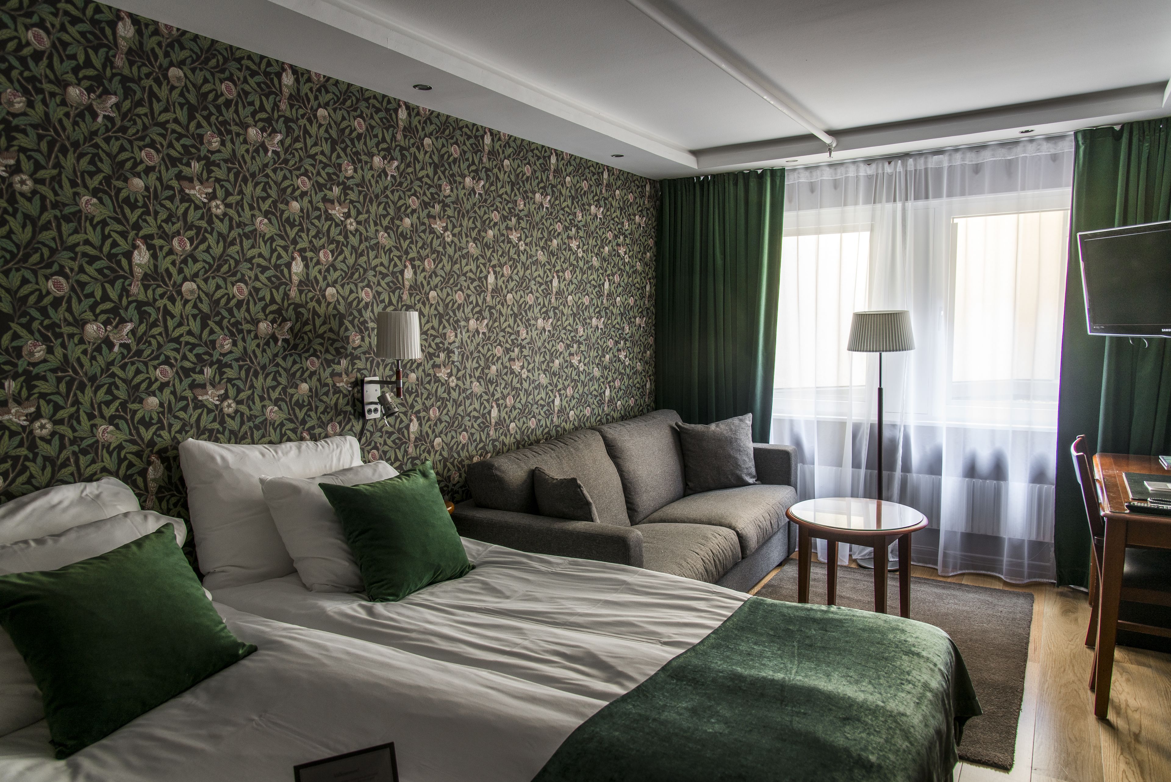 A hotel room with a large bed, a sofa, a small table, and a TV.