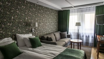 A hotel room with a large bed, a sofa, a small table, and a TV.