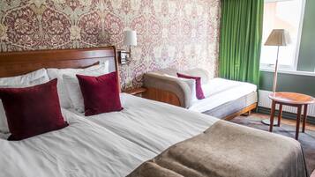 Une chambre d’hôtel avec deux lits, une tête de lit en bois, une table de chevet, une lampe et une vue sur l’extérieur par une fenêtre ornée de rideaux verts.