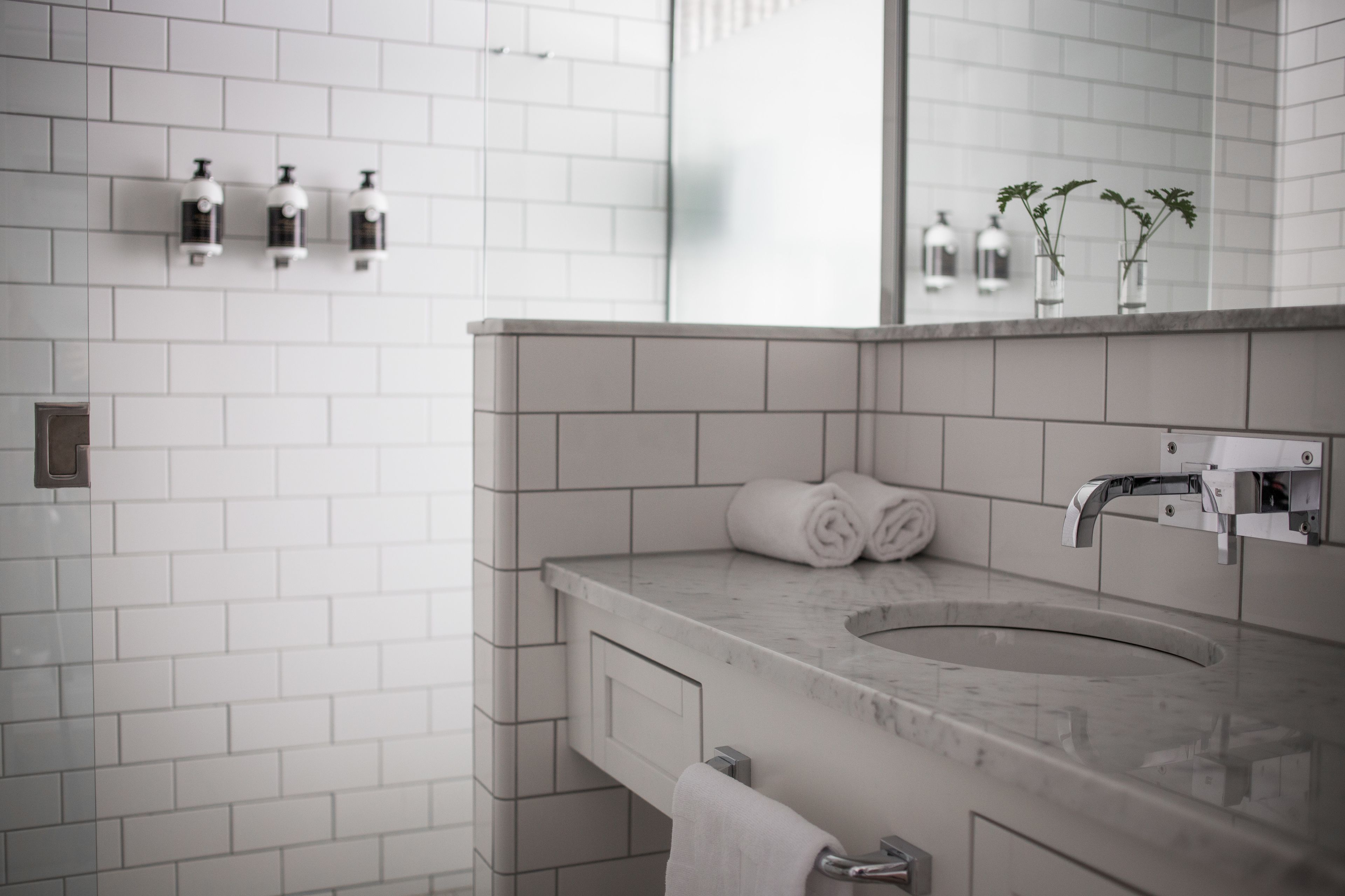 A modern bathroom with a marble sink, white tiles, a towel rack, and a mirror.