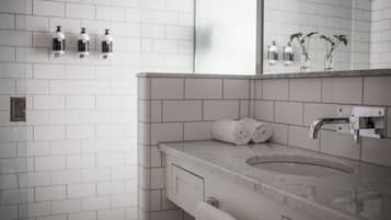A modern bathroom with a marble sink, white tiles, a towel rack, and a mirror.