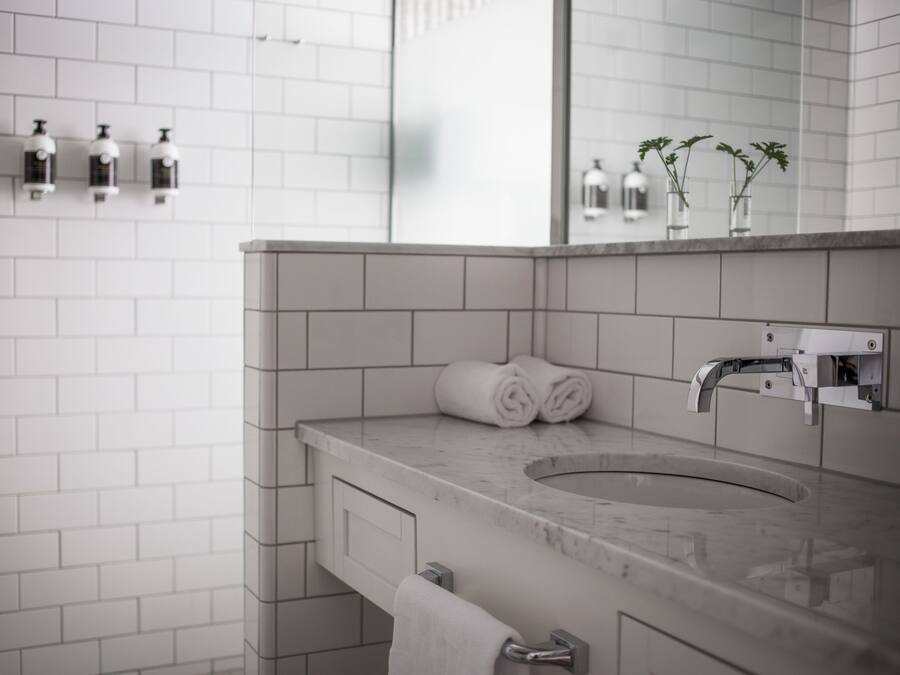 A modern bathroom with a marble sink, white tiles, a towel rack, and a mirror.
