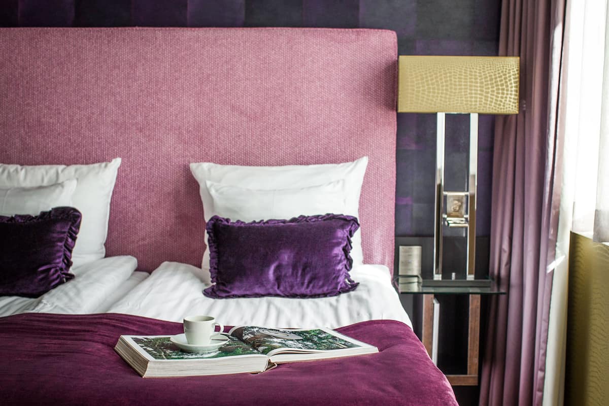 A neatly made bed with a purple bedspread, white pillows, and a book with a cup beside it.