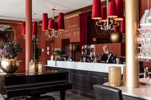 Welcome to our lobby, where a grand piano and beautiful flowers create a warm atmosphere. Guests can check in at the reception desk, which offers a telephone, cash register, and coffee machine.