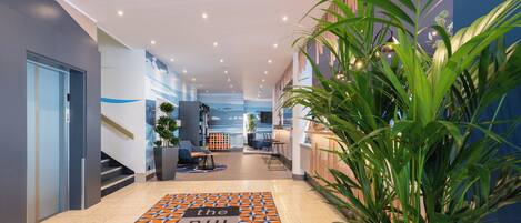 Un moderno vestíbulo de hotel con alfombra de diseño geométrico, un mostrador de recepción, una zona de estar y una escalera.