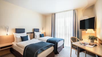 Habitación de hotel con dos camas, un escritorio, una silla, un televisor y una ventana con cortinas.