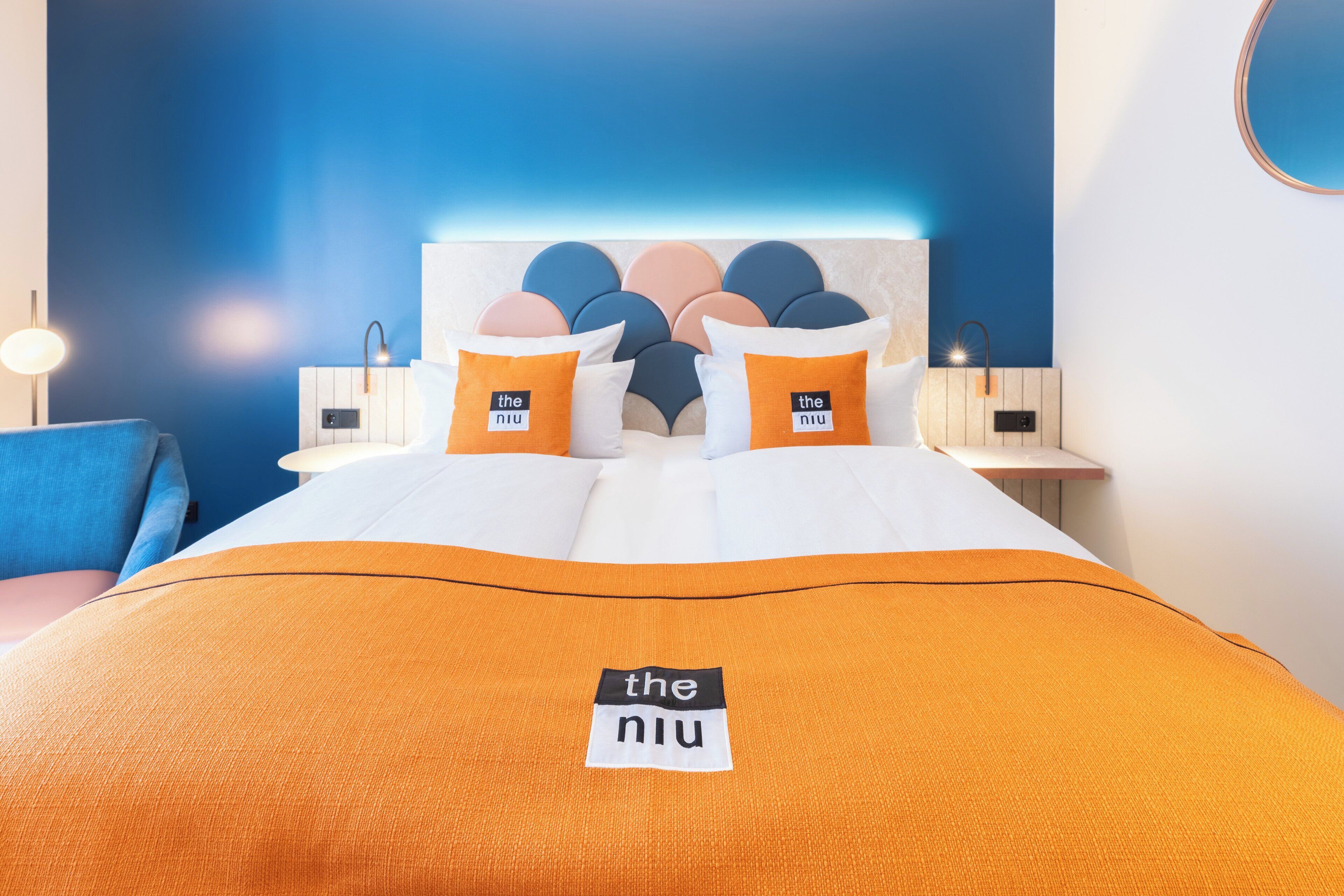 Habitación de hotel con cama, mesita de noche, lámpara y pared azul.