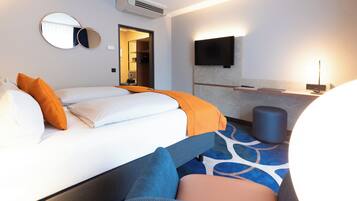 A hotel room with a bed, a TV mounted on the wall, a bedside table, and a bathroom visible through an open door.